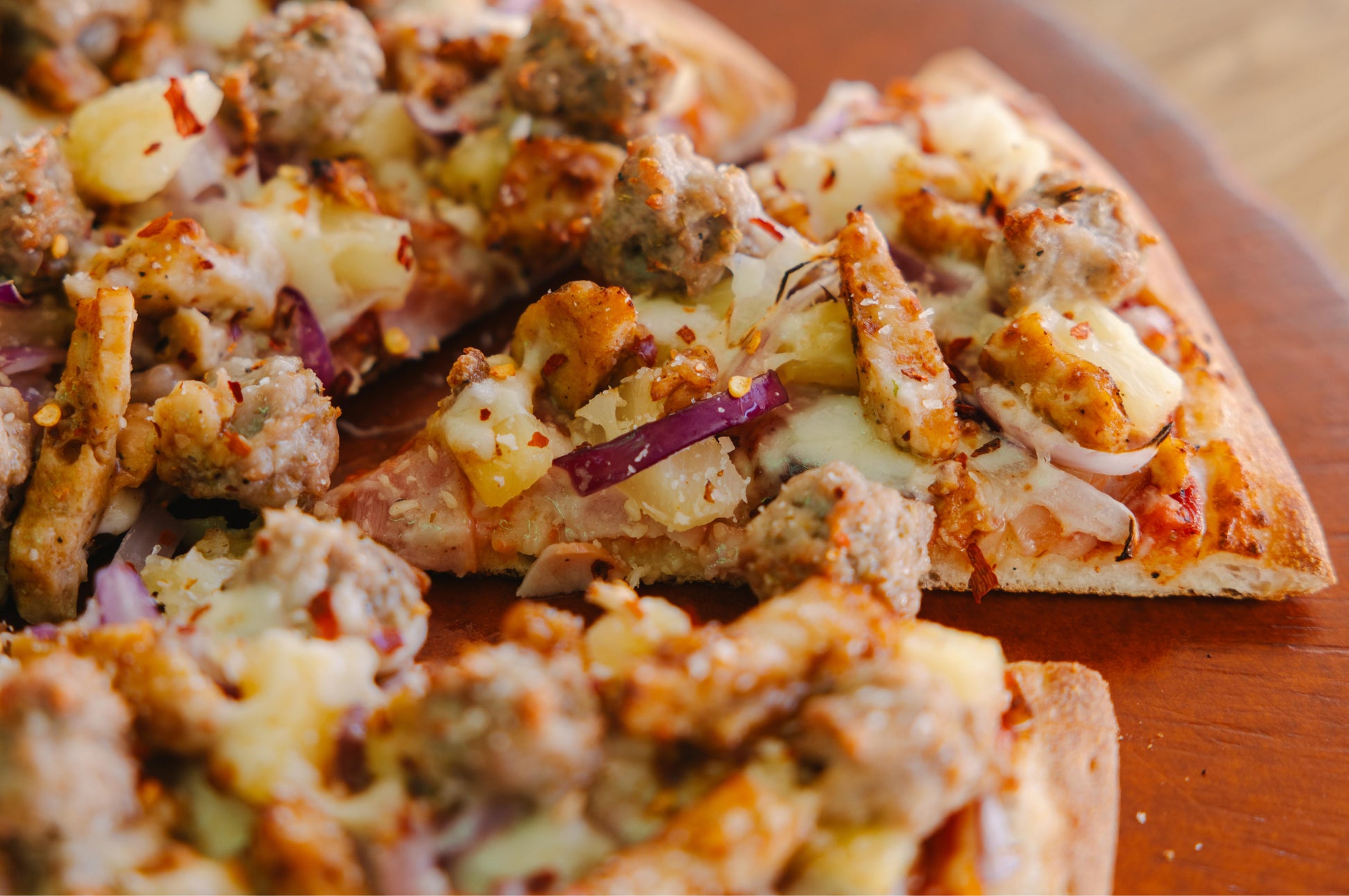Close-up of Hawaiian Supreme pizza with various toppings on a wooden surface
